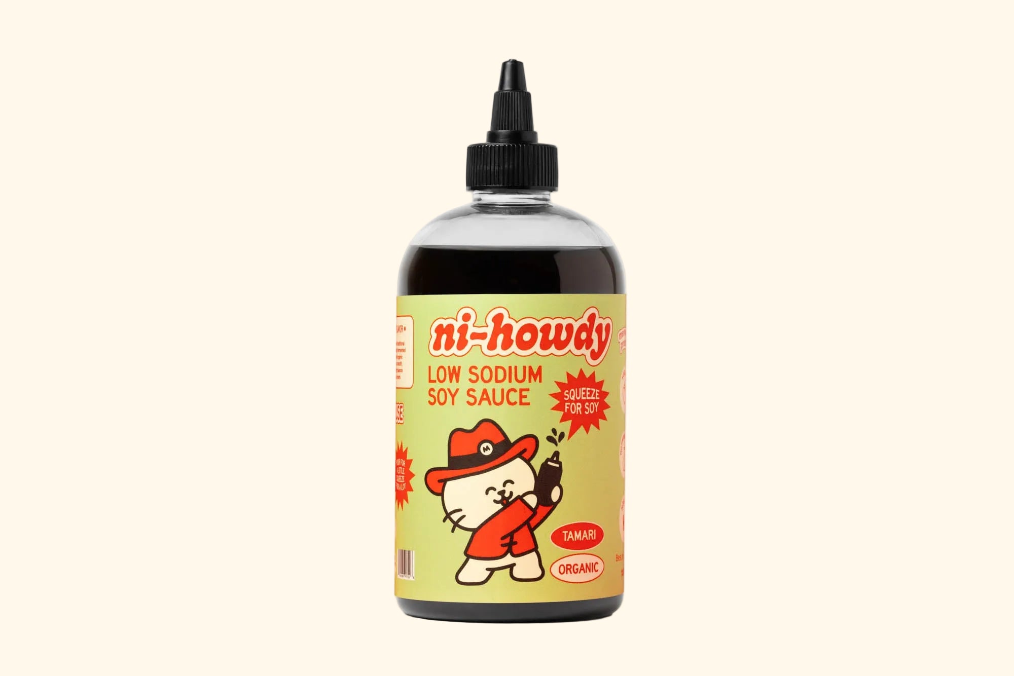 A bottle of ni-howdy brand low sodium soy sauce, featuring a black plastic squeeze cap and a light yellow label with a cartoon cat character wearing a red hat and jacket.